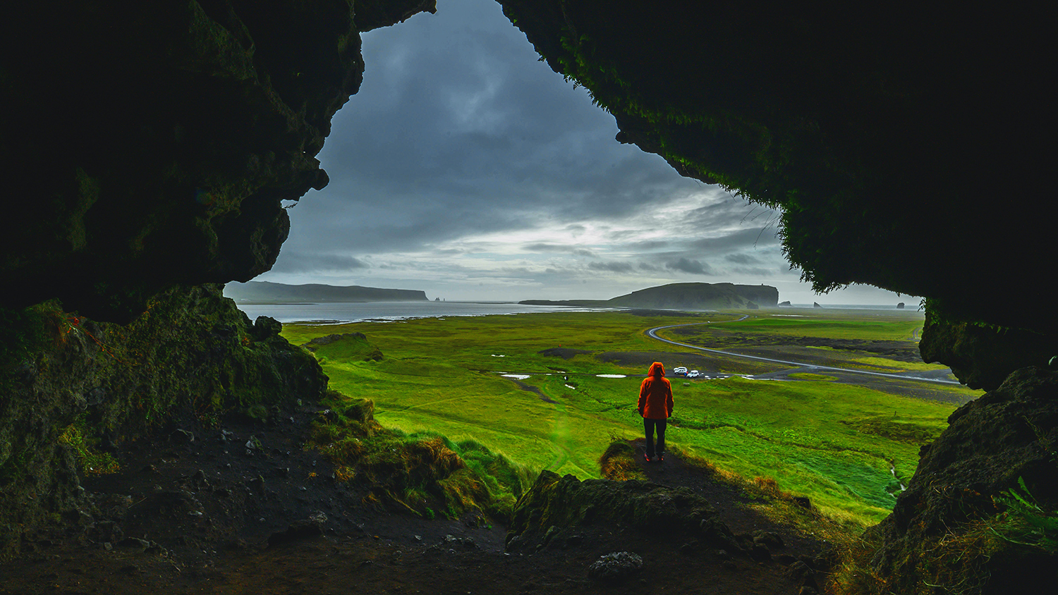 person standing in cave entrance overlooking huge landscape